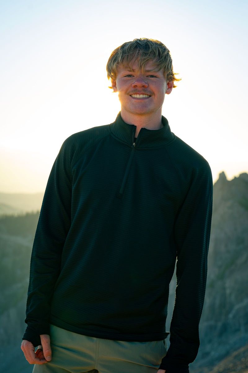 Austin Wessman smiling, backlit by a low sun on a rocky ridge