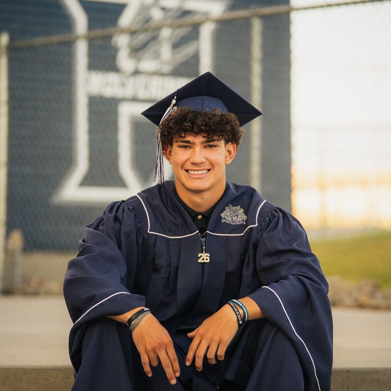 Graduate seated on steps with school logo fence behind