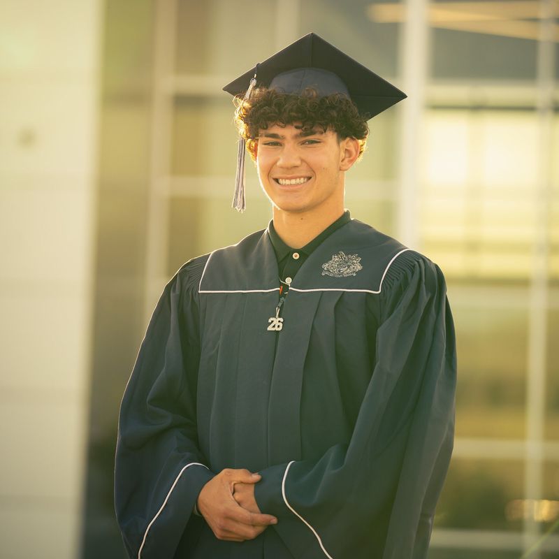 Graduate in cap and gown smiling, soft window glow behind