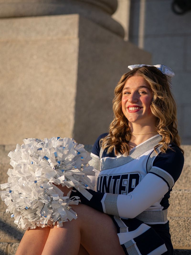 Cheerleader seated on stone steps holding white pom-poms in warm light