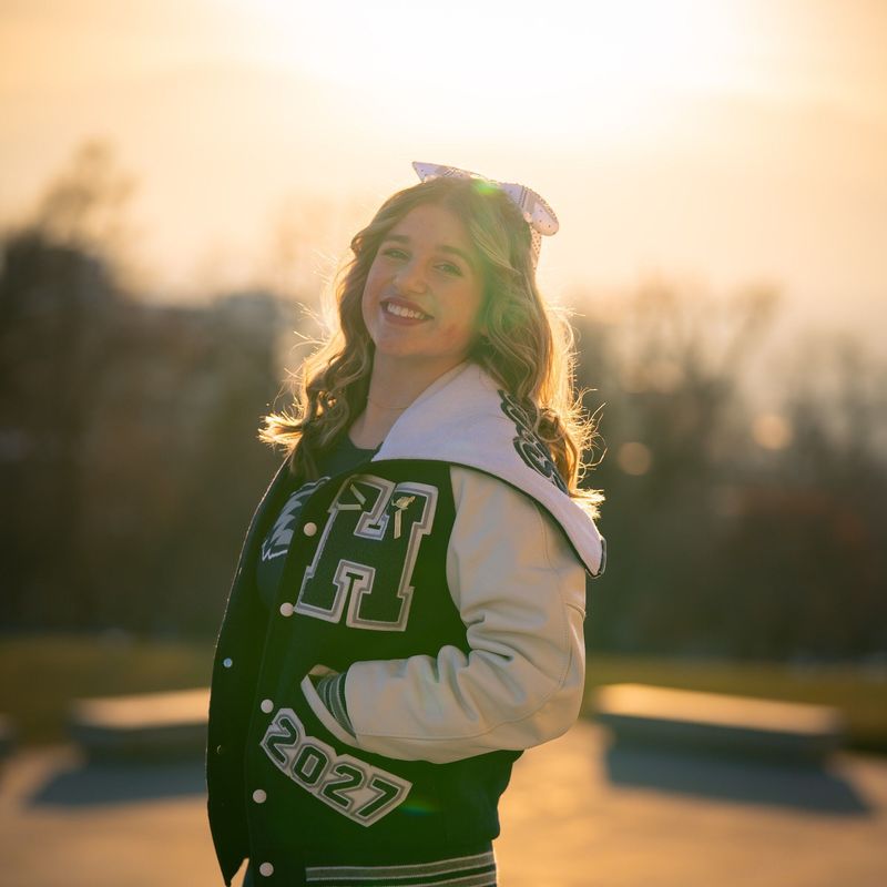 Cheerleader in a green letterman jacket against golden bokeh sunset
