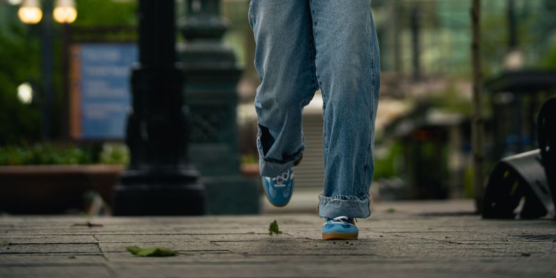 Close detail of jeans and blue sneakers mid-stride on a downtown sidewalk