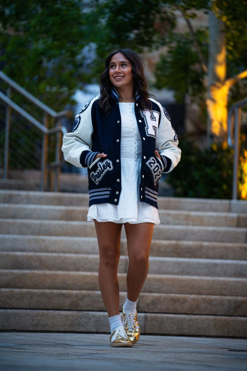 Senior in a letterman jacket walking down outdoor stairs between greenery