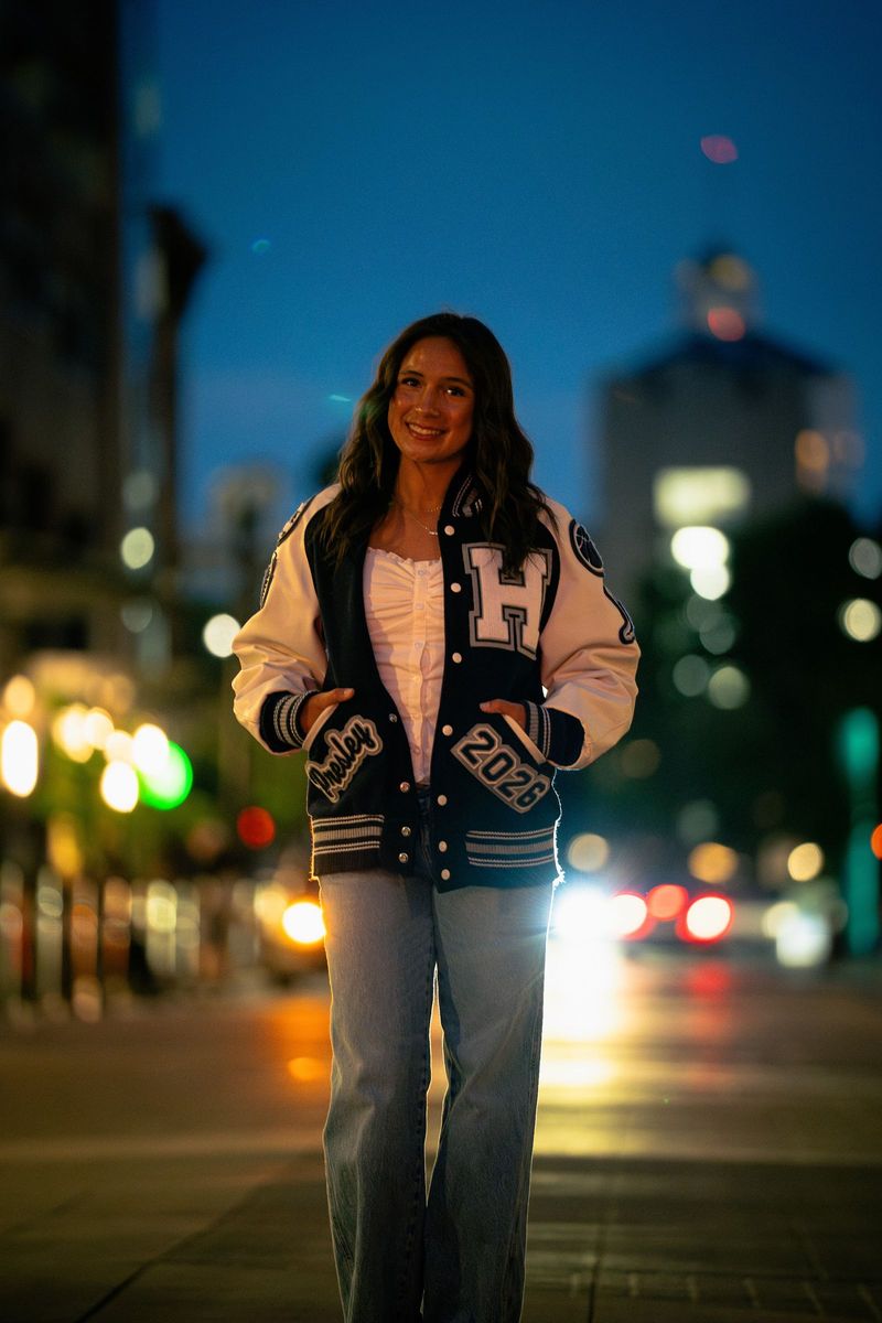 Senior in a letterman jacket on a street at blue hour with glowing signs