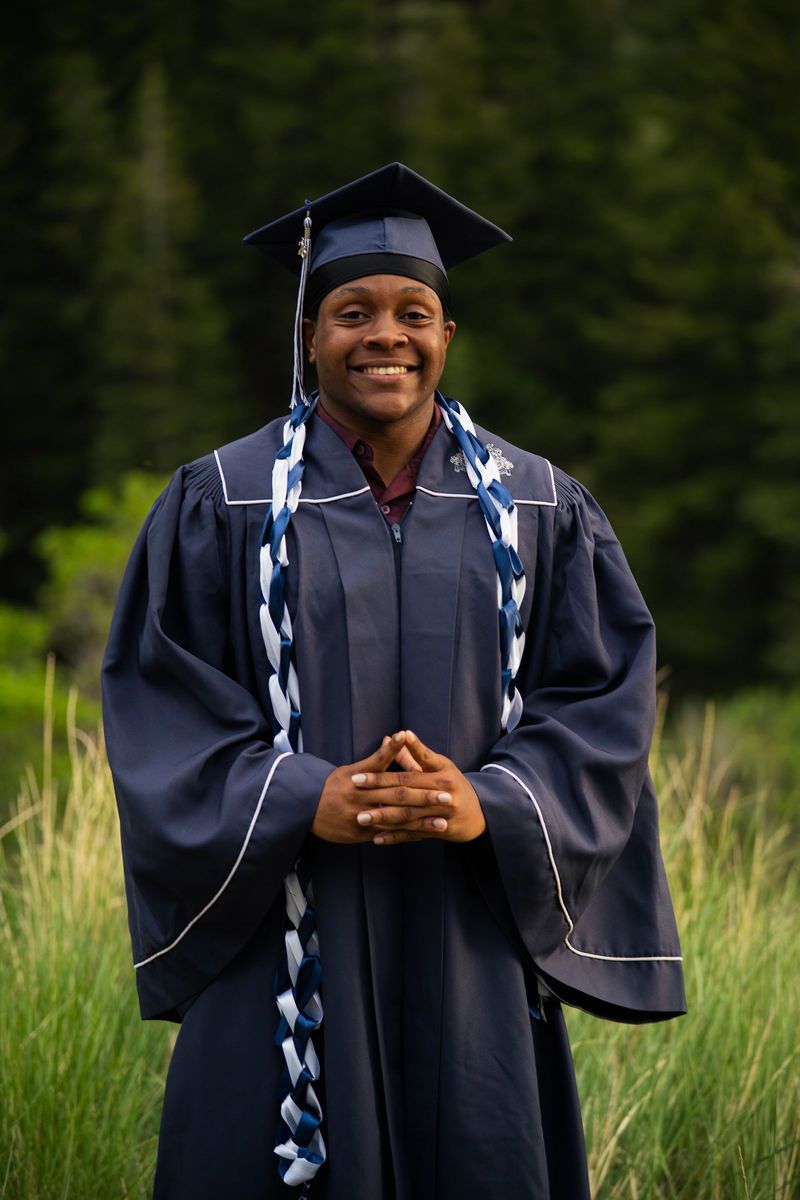 Graduate in cap and gown with hands together in a green meadow