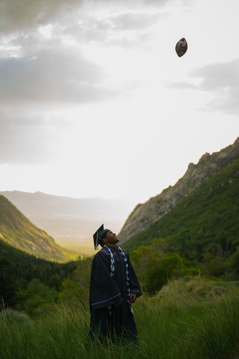 Graduate far below a mountain ridge with a football high in the sky